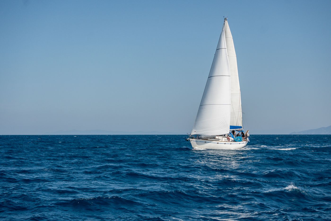 A sailing yacht with a white sail on the blue sea